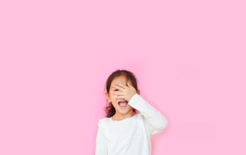 Attractive asian little kid girl peeking in shock covering face and eyes by hand.